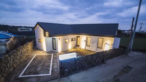 Une petite maison moderne avec une entrée surmontée d’un mur en pierre, une véranda bien éclairée et une allée dégagée.