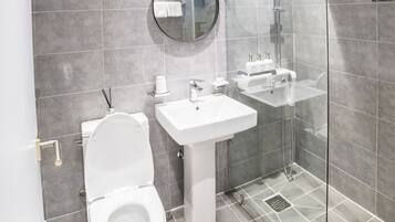 Un baño moderno con inodoro, lavamanos y cabina de ducha con mampara de vidrio.