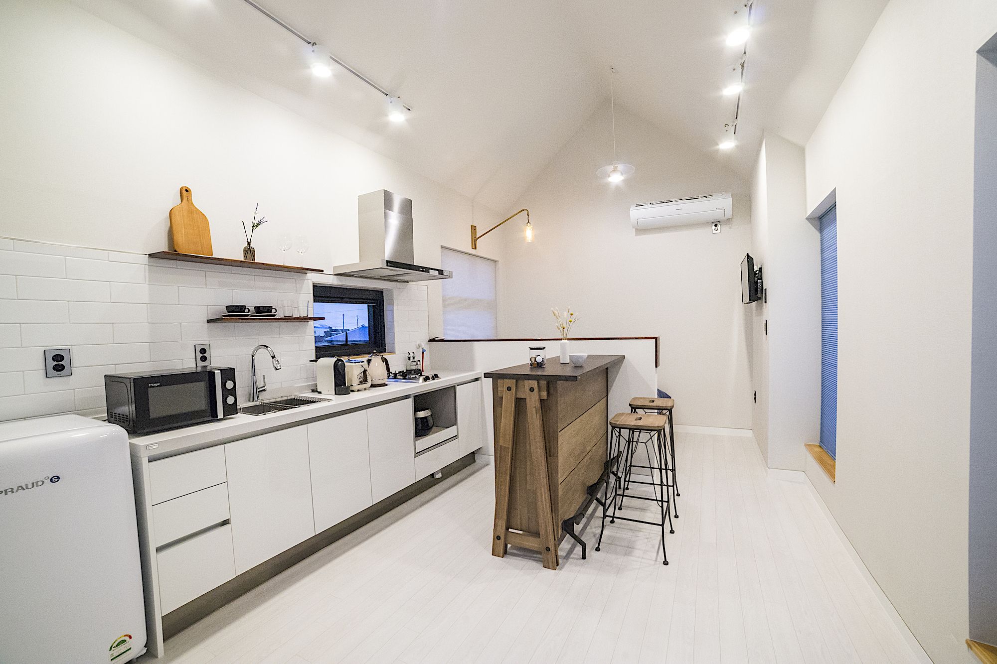 A modern kitchen with white cabinetry, a built-in microwave, a sink, and a wooden island with stools.