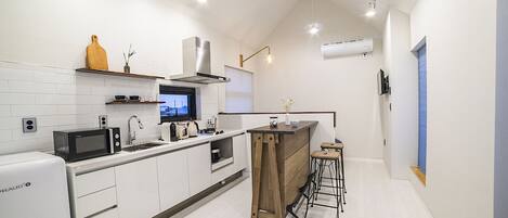 A modern kitchen with white cabinetry, a built-in microwave, a sink, and a wooden island with stools.
