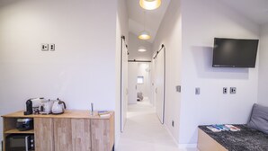 Une chambre d’hôtel moderne dotée d’un bureau en bois, d’un téléviseur à écran plat, d’un coin salon confortable et d’un couloir menant aux autres chambres.