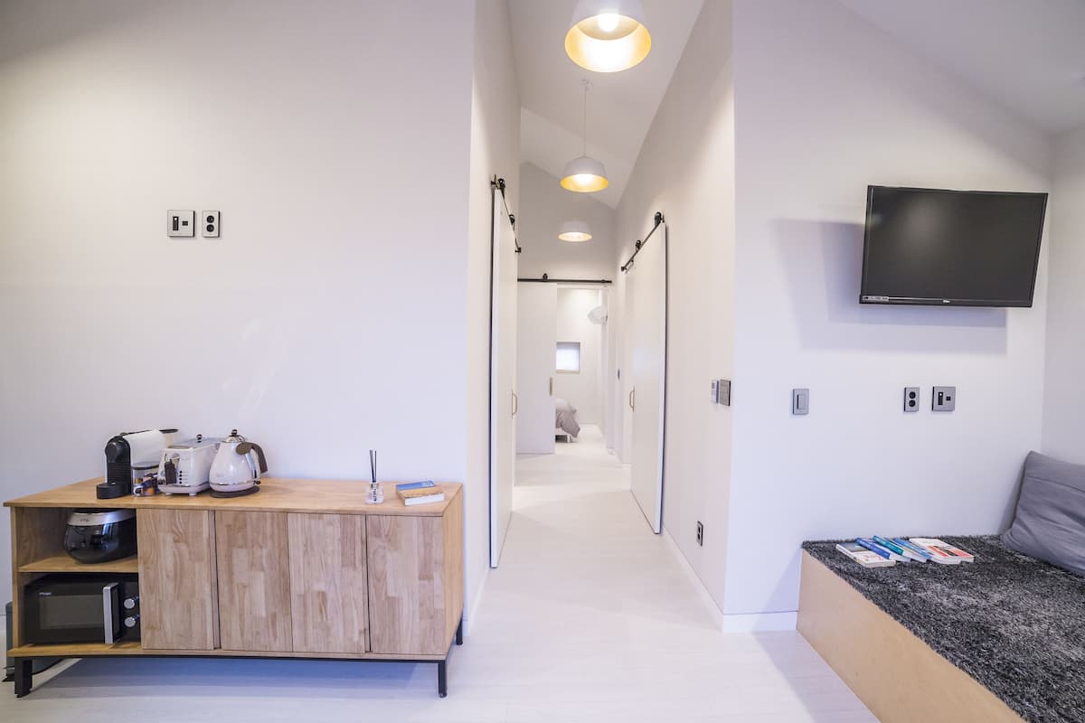 Une chambre d’hôtel moderne dotée d’un bureau en bois, d’un téléviseur à écran plat, d’un coin salon confortable et d’un couloir menant aux autres chambres.
