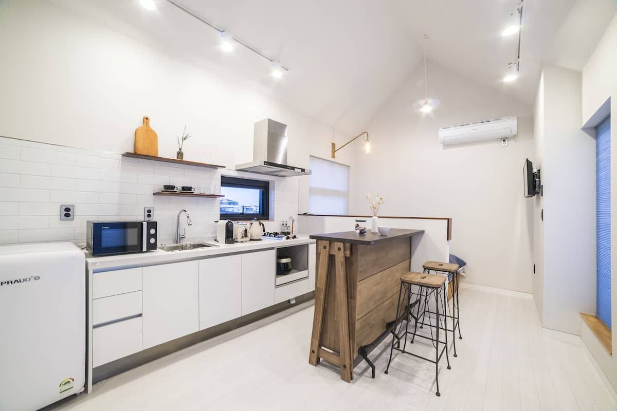 Une cuisine moderne avec des armoires blanches, un four à micro-ondes encastré, une hotte de cuisinière en acier inoxydable et un îlot central en bois avec des tabourets.