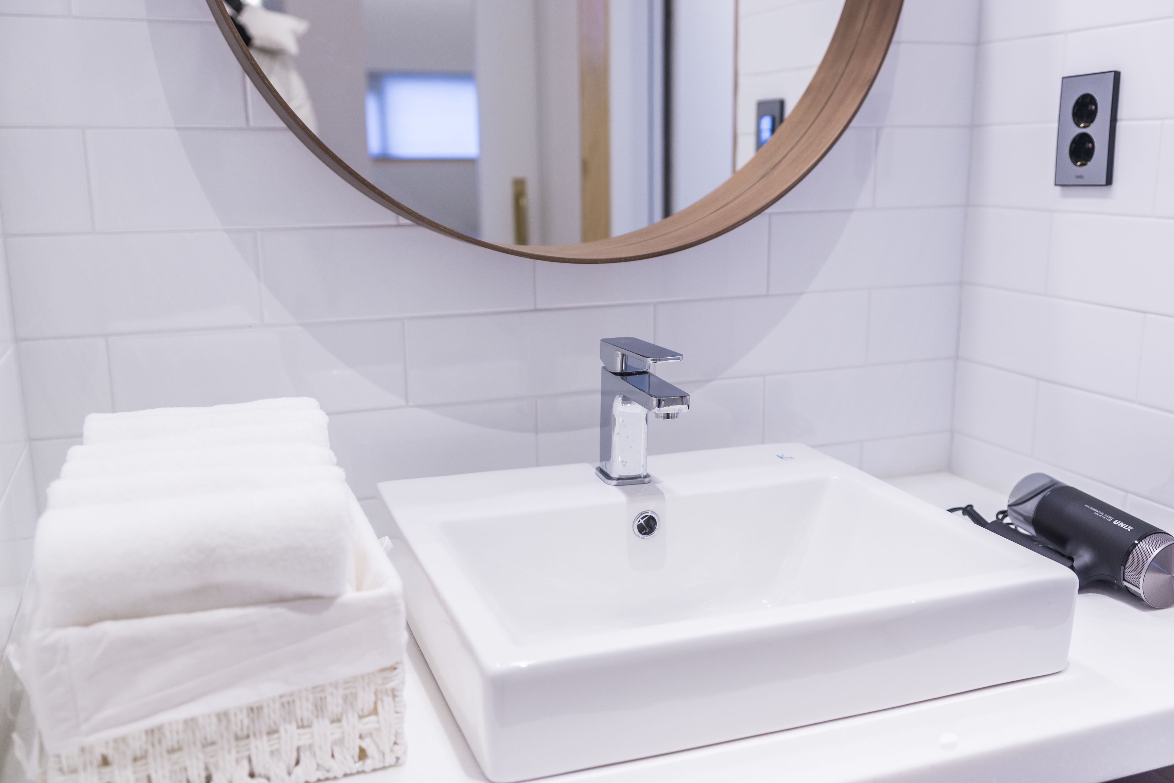 Une salle de bain avec un lavabo blanc, un miroir rond et un porte-serviettes.