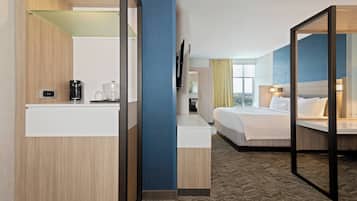 A hotel room with a bed, bedside table, and a mirror. There is a window with curtains and a view of the outside.