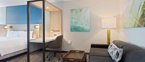 A hotel room with a bed, a desk, a chair, a sofa, and a tray table.
