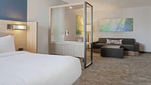Quarto de hotel com uma cama, uma secretária com cadeira, um sofá e um espelho grande.