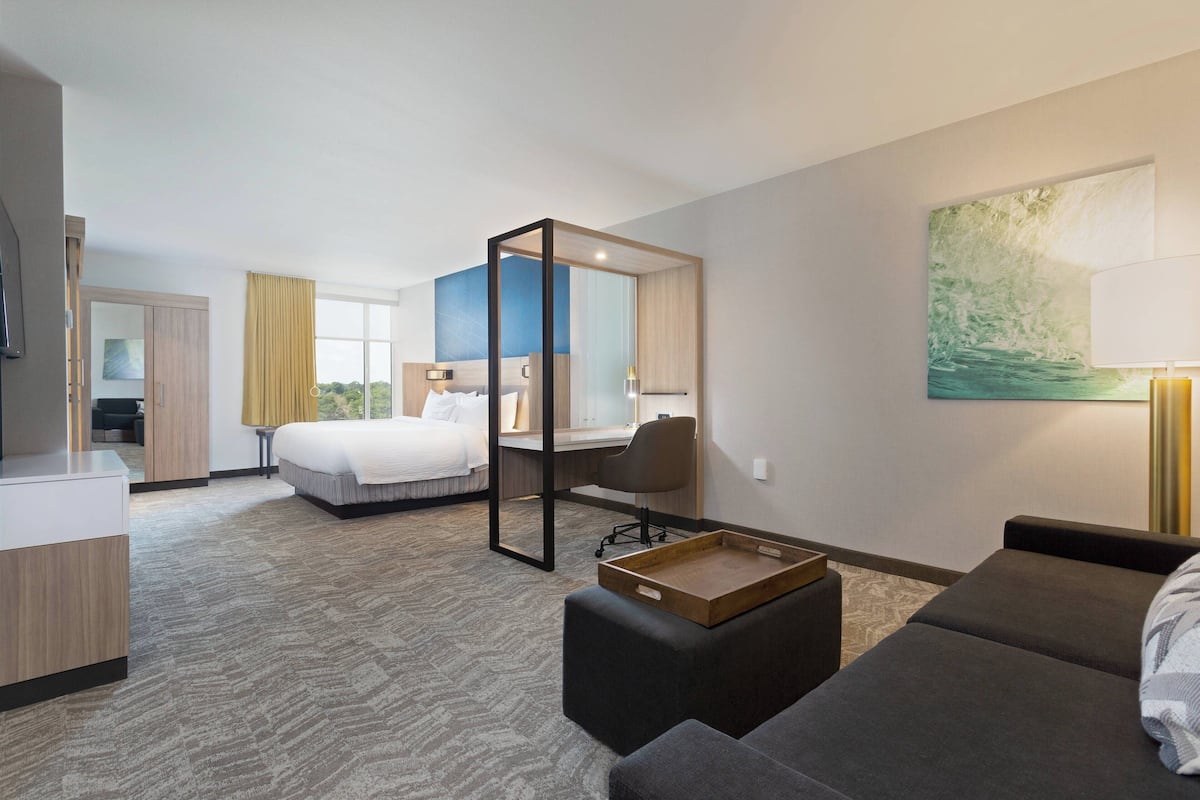 A hotel room with a bed, a desk, a chair, a sofa, and a painting on the wall.
