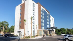 Um hotel moderno com fachada branca e marrom, vários andares e uma área de entrada coberta.