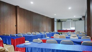 Une salle de conférence avec des rangées de tables, des chaises et une estrade.