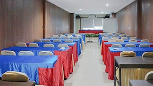Une salle de conférence avec des rangées de tables et de chaises, un pupitre et un grand écran à l’avant.