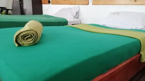 A single bed with a green bedspread and a rolled towel on it. - Foret De Vill - Hostel (Ella)