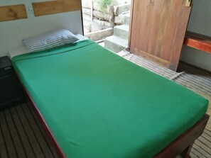 A single bed with a green mattress and a striped pillow in a room with wooden headboards and a view of a garden outside. - Foret De Vill - Hostel (Ella)