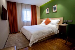 Een hotelkamer met een bed, een bureau, een stoel, een televisie en een raam met gordijnen.