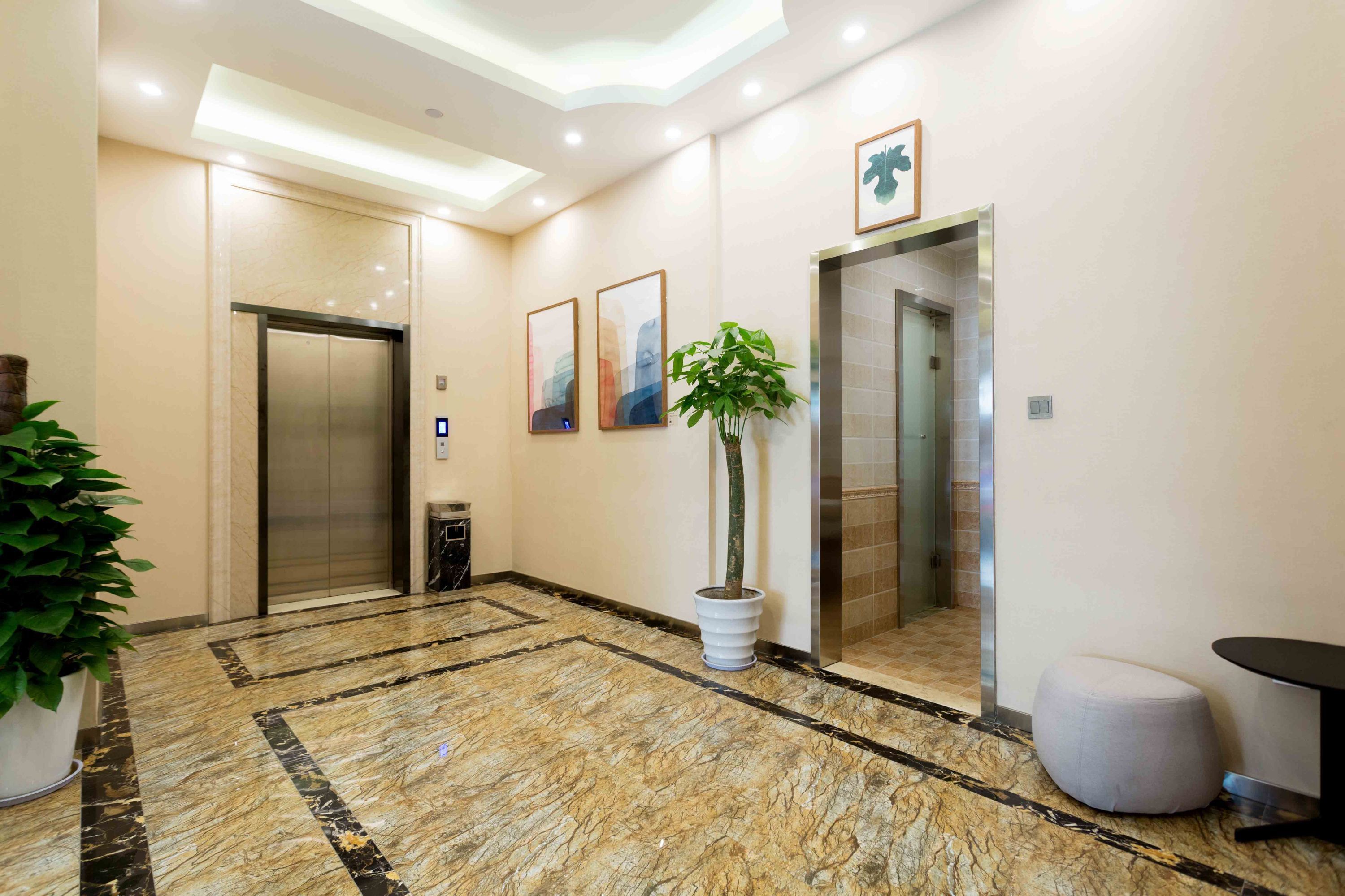 Un vestíbulo de hotel moderno con suelo de mármol, dos ascensores, una planta en maceta y un área de estar circular.