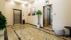 A modern hotel lobby with marble flooring, two elevators, a potted plant, and a round seating area. - Sucha Hotel Xian Bell Tower Huimin St (Xi'an)