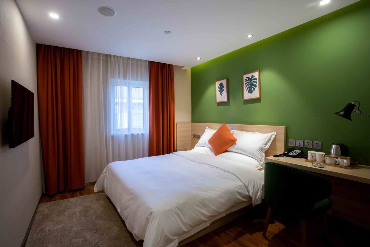 Ein Hotelzimmer mit Bett, Schreibtisch, Stuhl, Fernseher und einem Fenster mit Vorhängen.