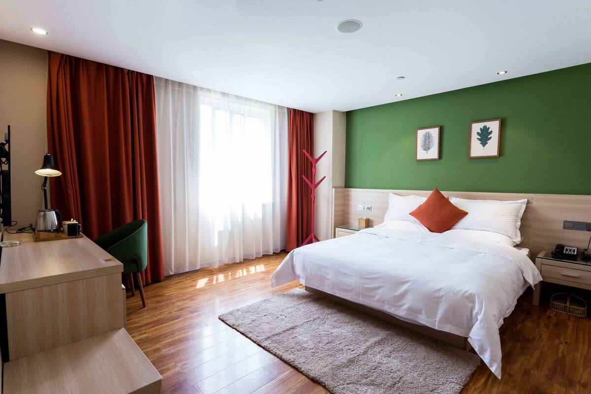 Ein Hotelzimmer mit Bett, Schreibtisch, Stuhl und einem fenster mit Vorhängen.