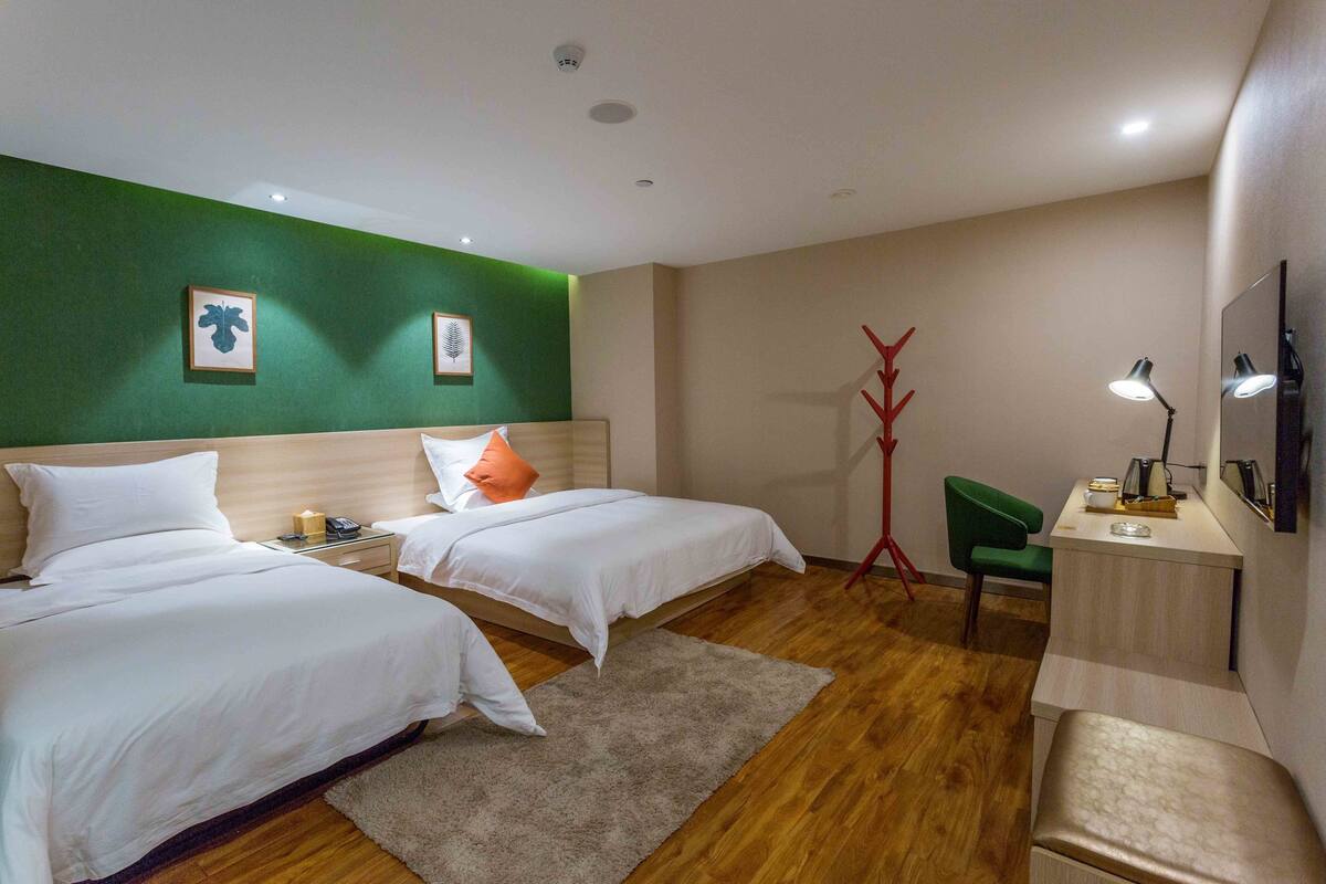 Ein Hotelzimmer mit zwei Betten, einem Schreibtisch, einem Sessel, einem Fernseher und einem roten Kleiderhaken.