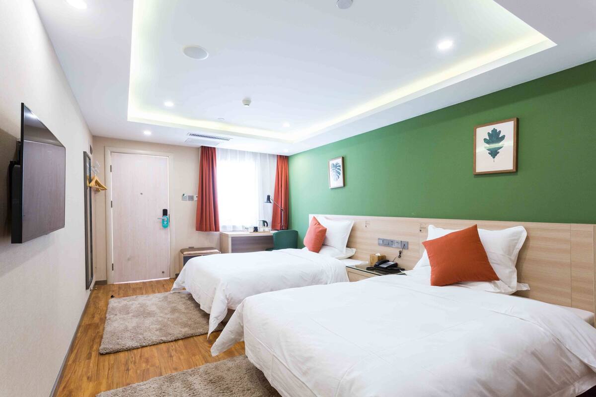 Ein Hotelzimmer mit zwei Betten, einem Fernseher, einem Schreibtisch und einer grünen Wand.