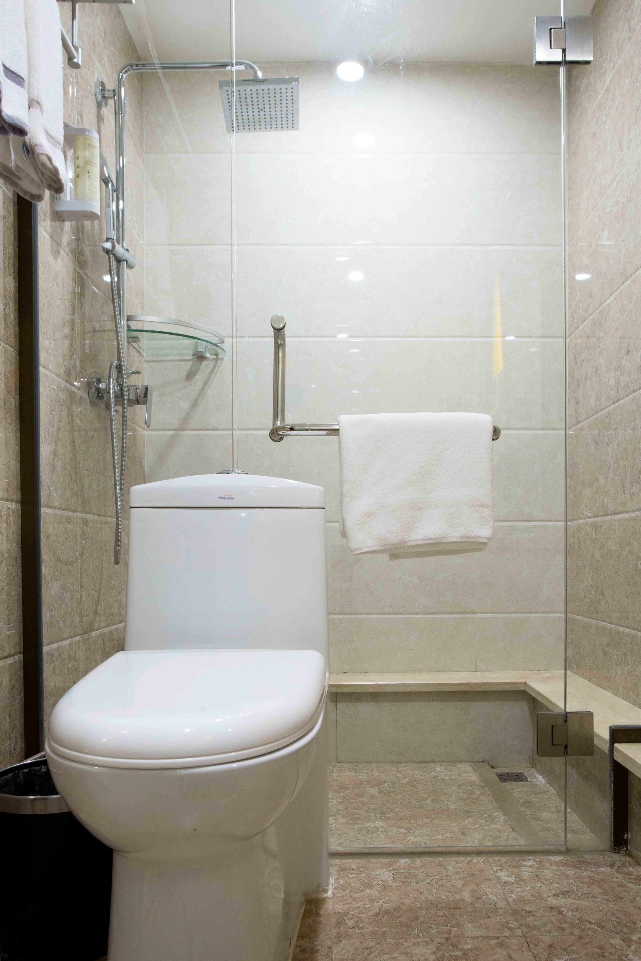 A modern bathroom with a glass-enclosed shower, a white toilet, and a glass shelf with toiletries.