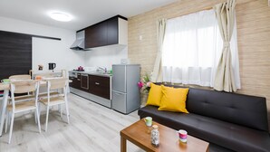 A modern kitchen with a dining area, a sofa with yellow cushions, and a window with curtains. - Mikazuki House Teradacho (Osaka)