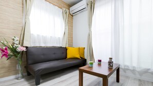A modern living room with a dark sofa, a wooden coffee table, and a vase of flowers. - Mikazuki House Teradacho (Osaka)