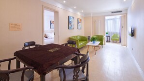 Une chambre d’hôtel comprenant un coin repas, un canapé vert, une petite table avec une plante et un lit avec une literie blanche.