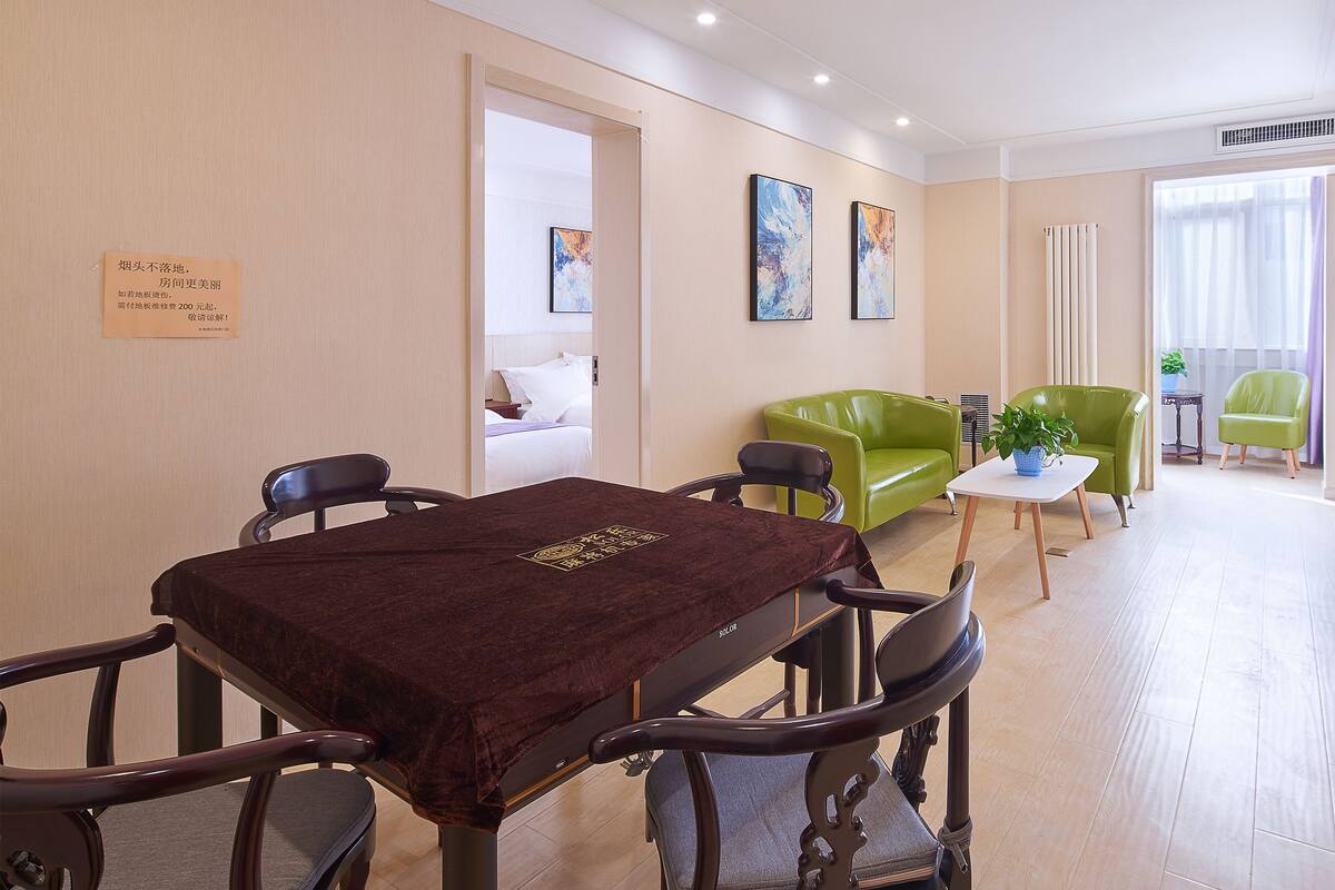 A hotel room with a dining area, a green sofa, a small table with a plant, and a bed with white bedding.