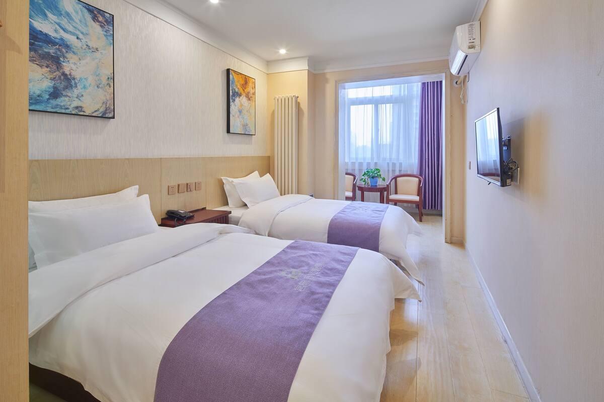 A hotel room with two beds, a TV, a window with curtains, and a small table with chairs.