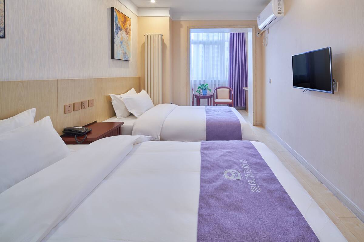 A hotel room with two beds, a TV, a desk with a phone, and a view of the outside.