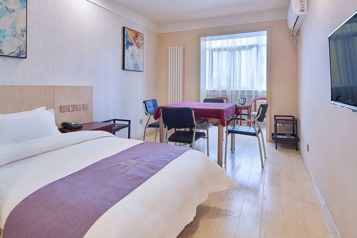 A hotel room with a bed, a desk, a chair, a table, and a TV.