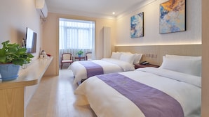 Une chambre d’hôtel avec deux lits, un bureau agrémenté d’une plante, une chaise, une fenêtre avec des rideaux et des œuvres d’art accrochées au mur.