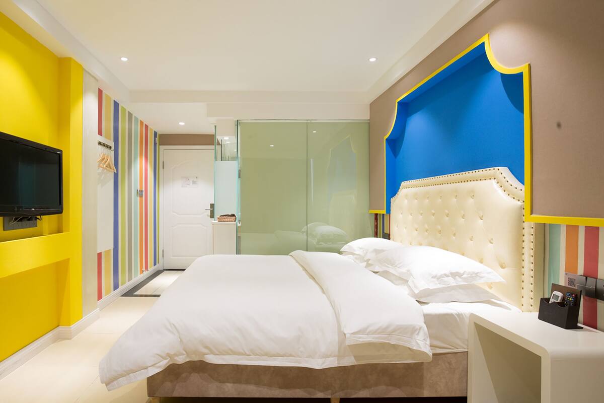 A modern bedroom with a bed, a television, and a glass door leading to a bathroom.