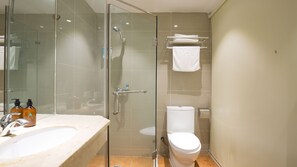 Un baño moderno con ducha envuelta en vidrio, inodoro blanco y tocador con lavamanos y dispensadores de jabón.