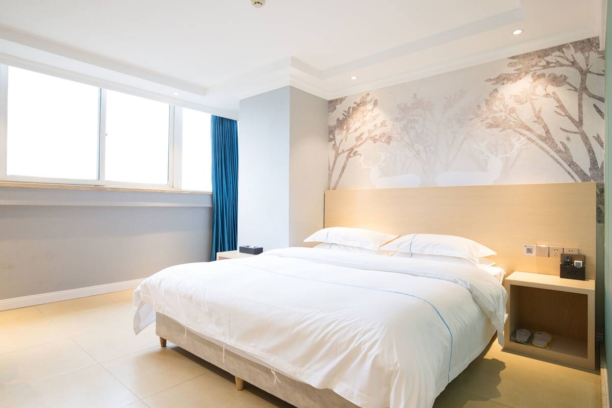 A modern hotel room with a large bed, a nightstand with a lamp, and a wall-mounted artwork.