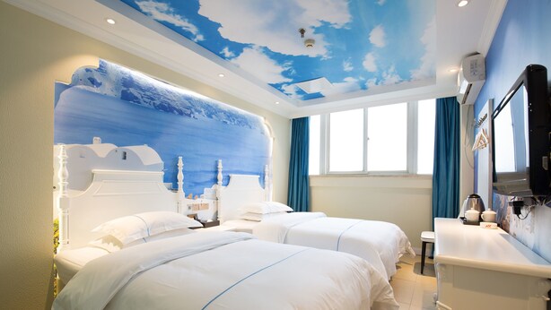 A hotel room with two beds, a large mural of a blue sky and white clouds, a window with blue curtains, and a white vanity with a mirror. - Sucha Hotel Chongqing Jiefangbei (Chongqing)