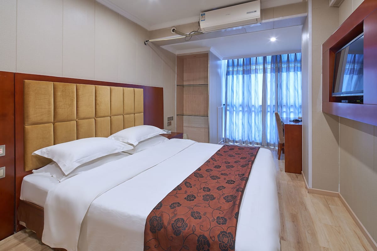 A hotel room with a large bed, a TV mounted on the wall, and a window with curtains.