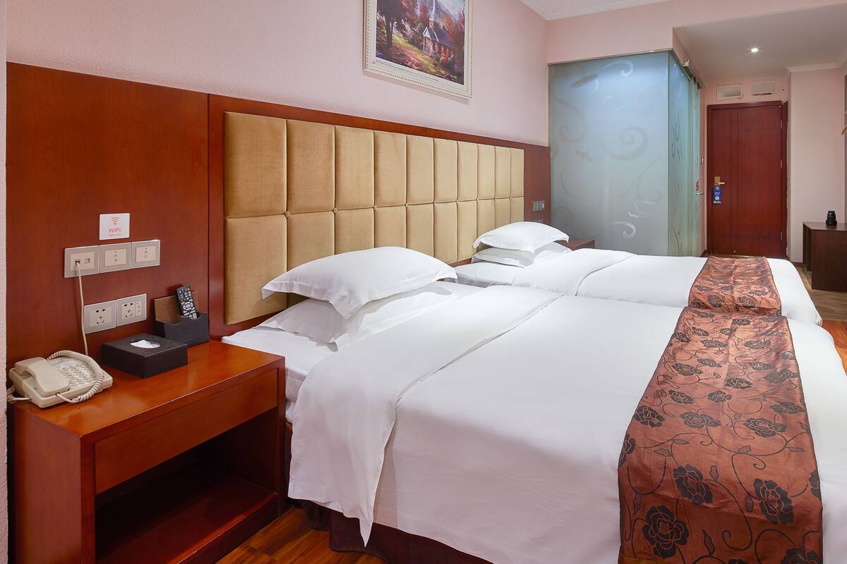 A hotel room with a large bed, a bedside table with a phone, a lamp, and a picture on the wall.