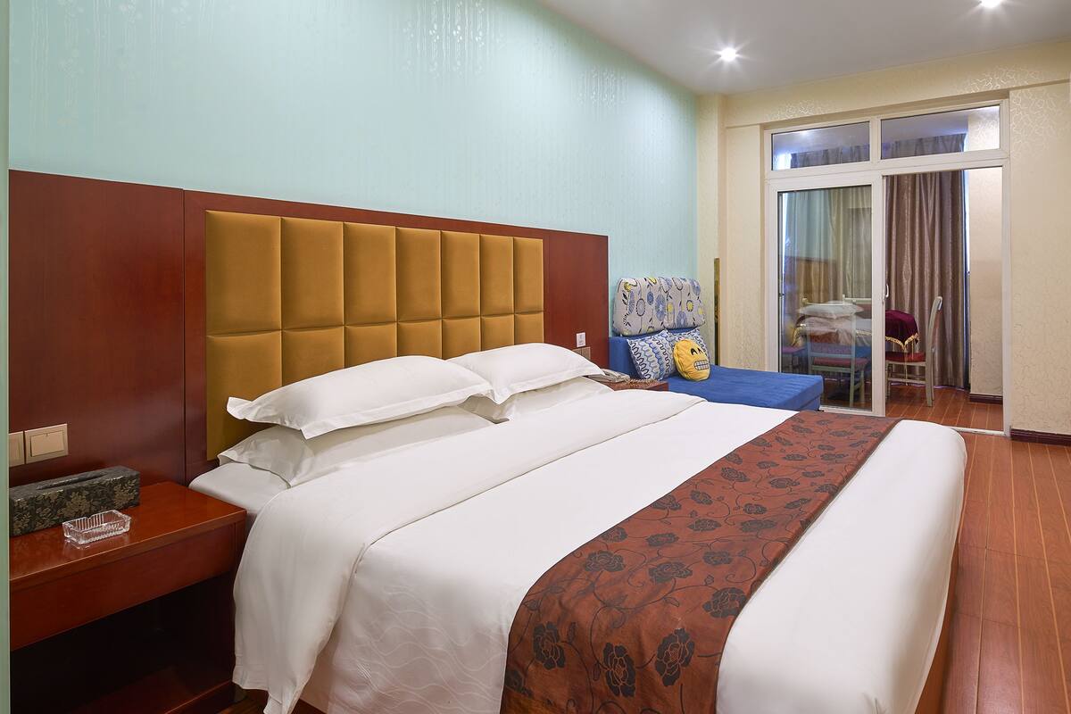 A hotel room with a large bed, a bedside table, a chair, a TV, and a sliding glass door leading to a balcony.