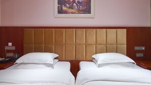 Habitación de hotel con un gran cabecero acolchado, dos camas con sábanas blancas, un cuadro sobre el cabecero y un revestimiento de pared de madera.