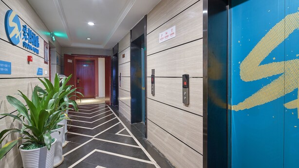 A hotel corridor with a modern design, featuring a patterned floor, potted plants, and a blue elevator with a distinctive logo. - Sucha Hotel Chongqing N. Railway Station (Chongqing)