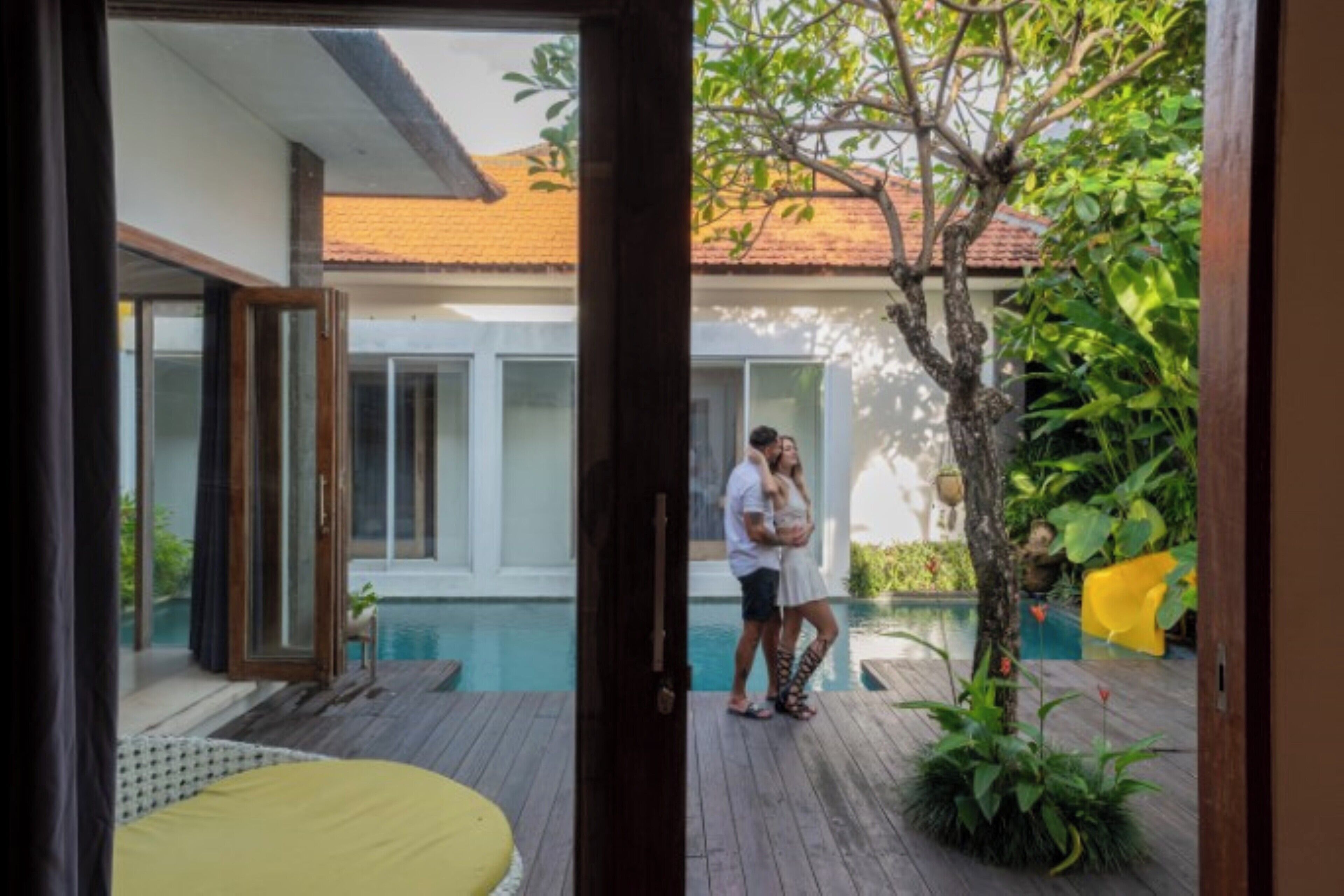 A wooden deck with a pool, a tree, and a yellow chair.