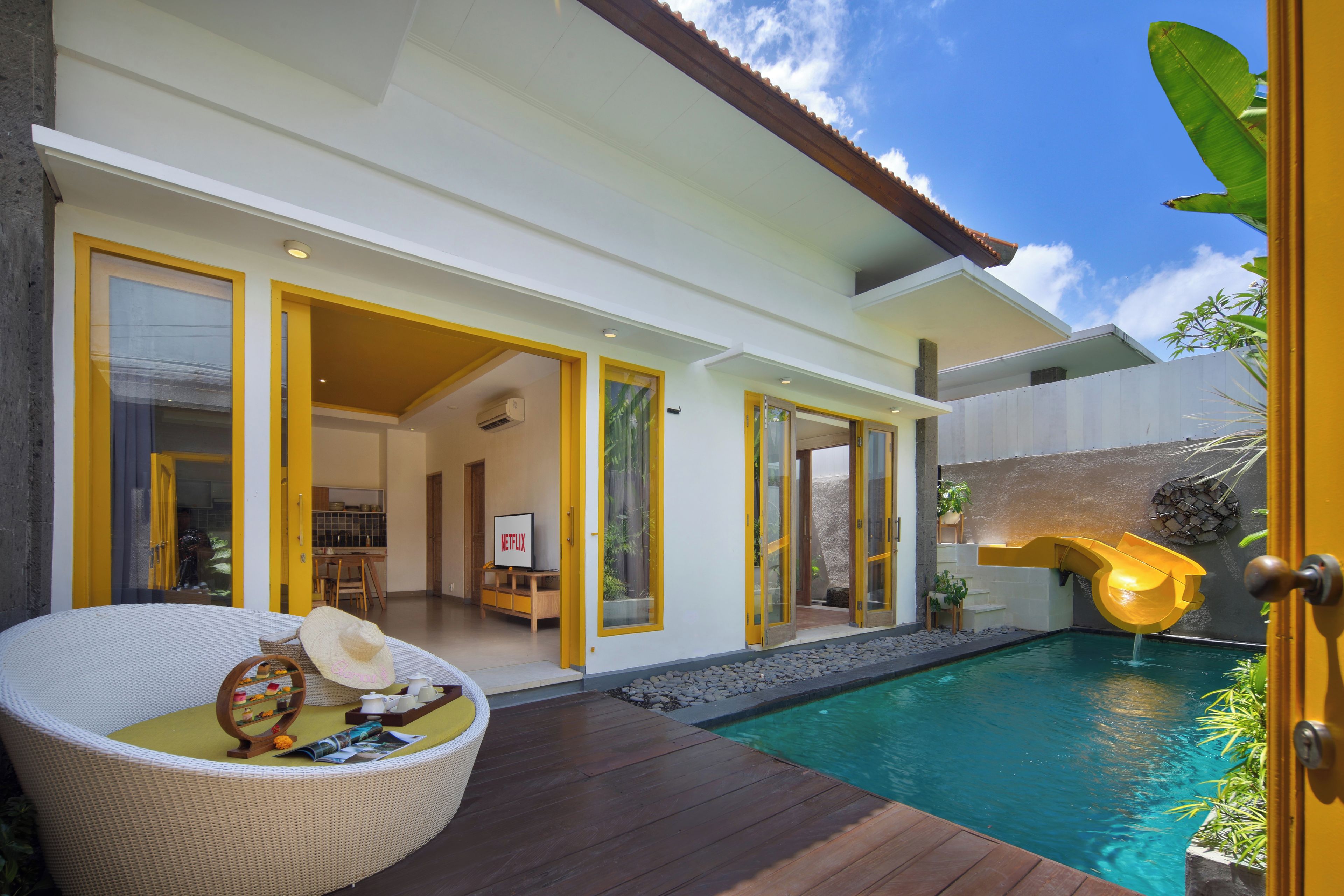 A modern house with a swimming pool, a dining area, and a kitchen visible through the open doors.