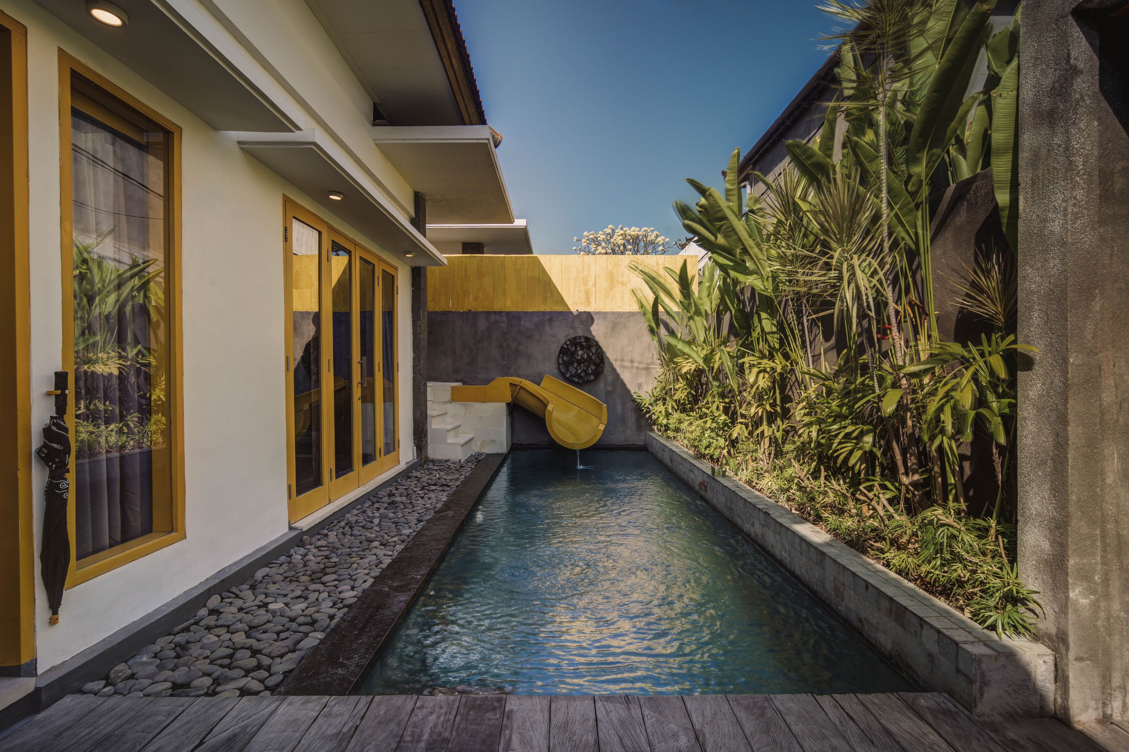 A pool area with a water slide, surrounded by tropical plants and a stone wall.