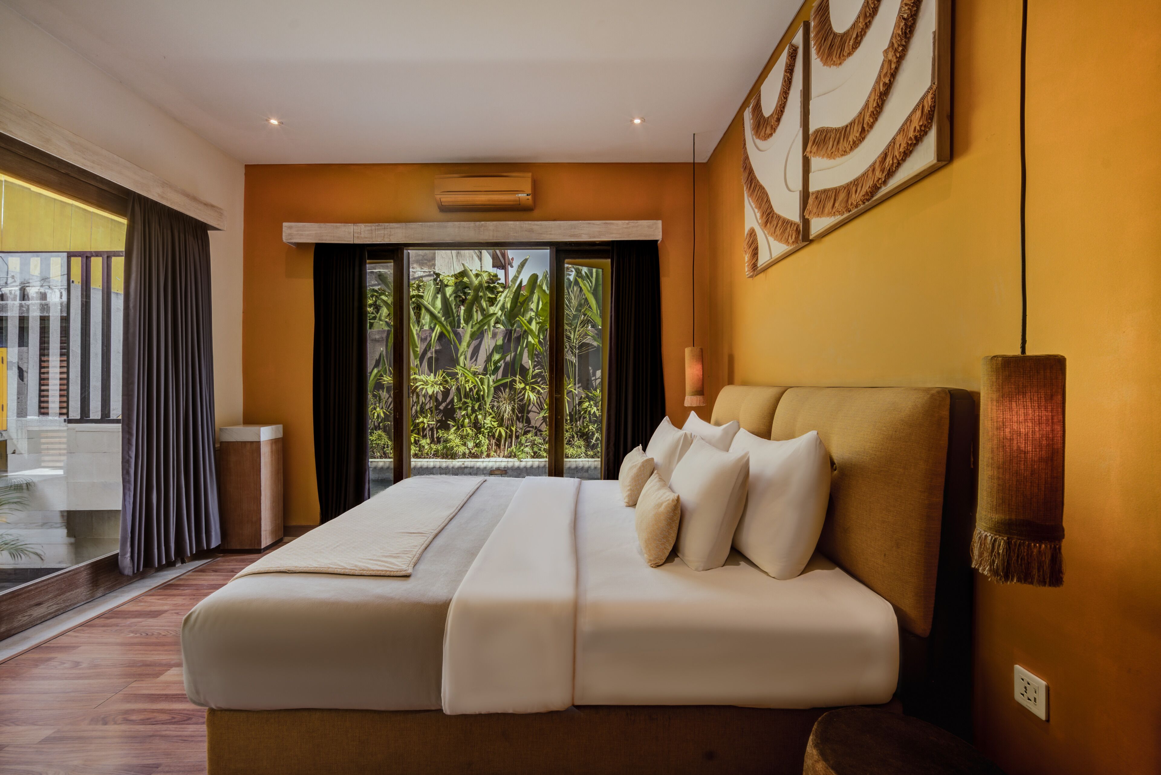 Habitación de hotel con una cama grande, vista a través de la puerta de cristal y una planta tropical visible en el exterior.