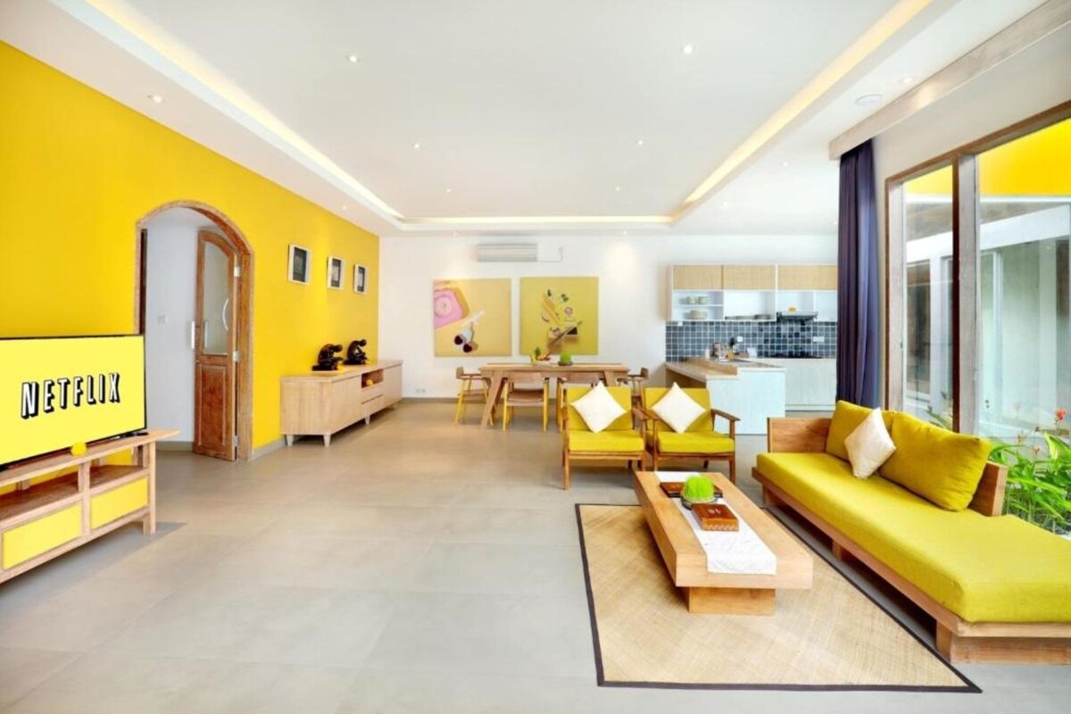 A modern living room with a yellow wall, a dining area, and a kitchen.
