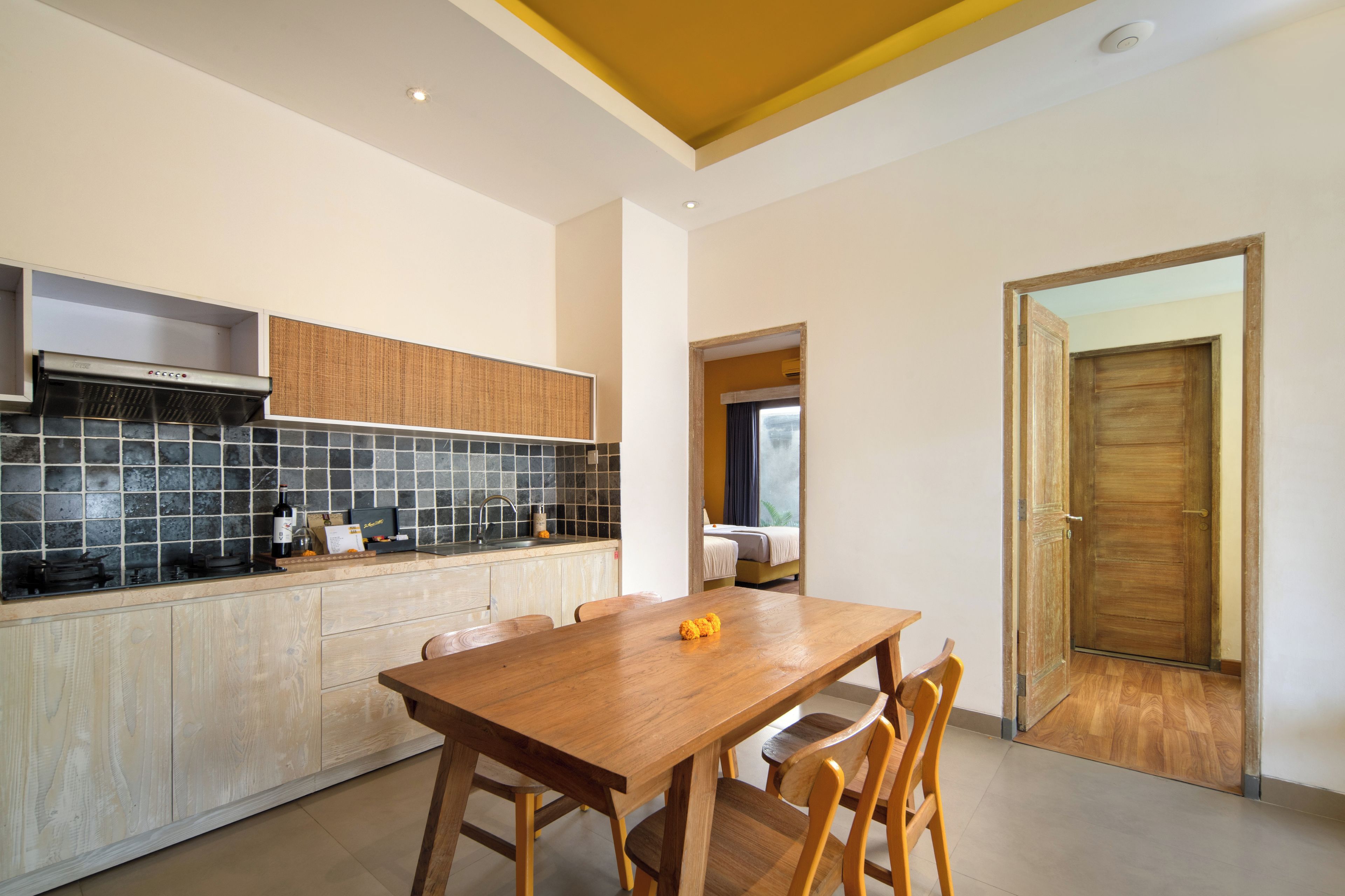 A modern kitchen with a dining area, featuring a wooden table and chairs, a built-in stove, and a tiled backsplash.