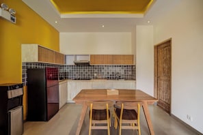 A modern kitchen with a wooden dining table, two chairs, a refrigerator, and a stove. - La Mira Villa Seminyak by Ini Vie Hospitality (Kerobokan)