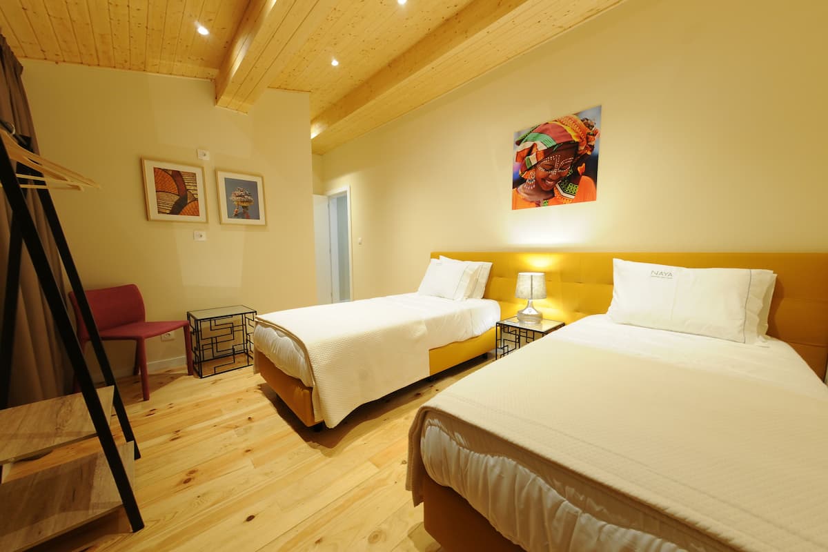 Habitació d'hotel amb dos llits, terres de fusta, una cadira vermella i un quadre a la paret.